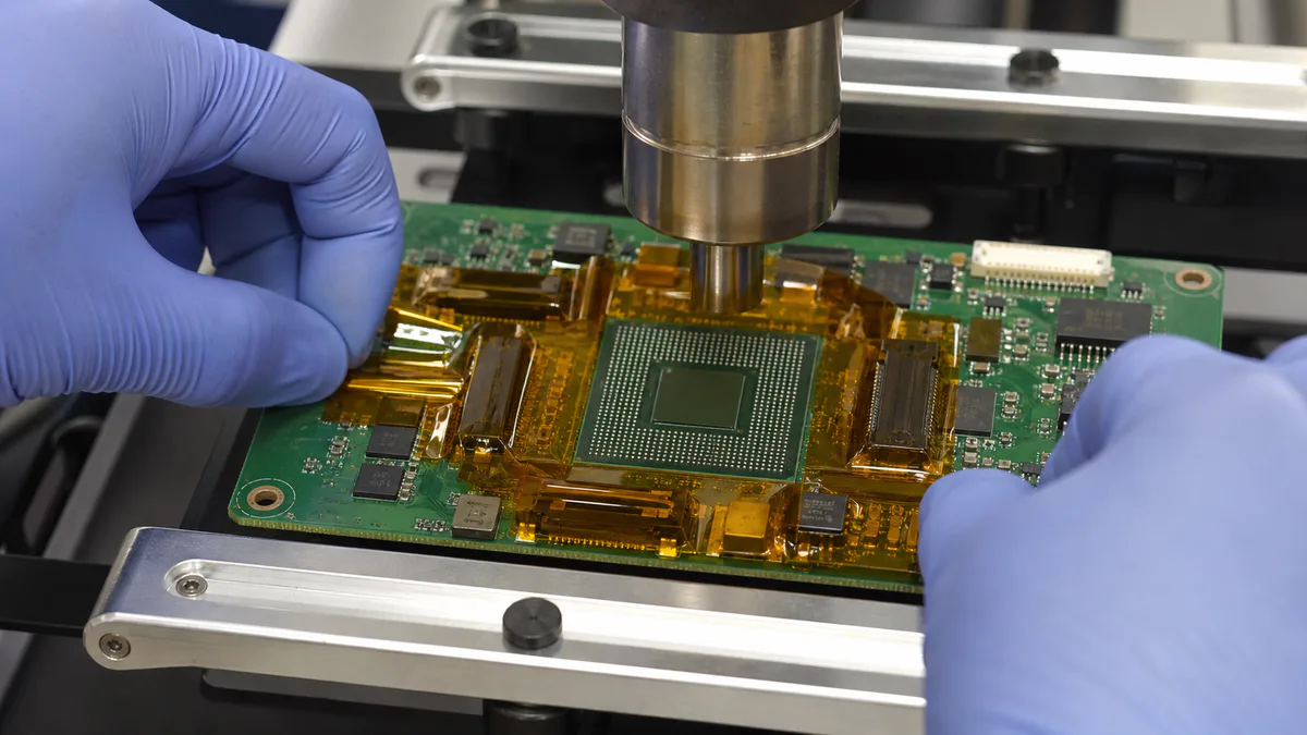 Electronics rework technician applying amber polyimide tape around adjacent PCB components before BGA hot-air rework
